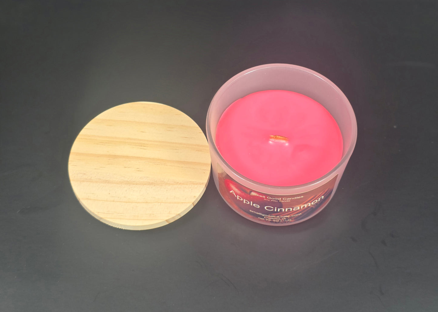 Pink candle in a clear container with a wooden lid on a dark background