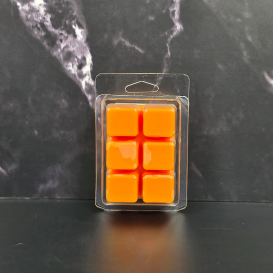 Pack of six orange wax melts in clear packaging on a dark marble surface