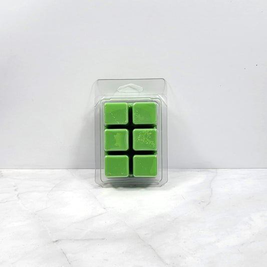 Pack of green wax melts in a clear plastic packaging on a white marble surface.