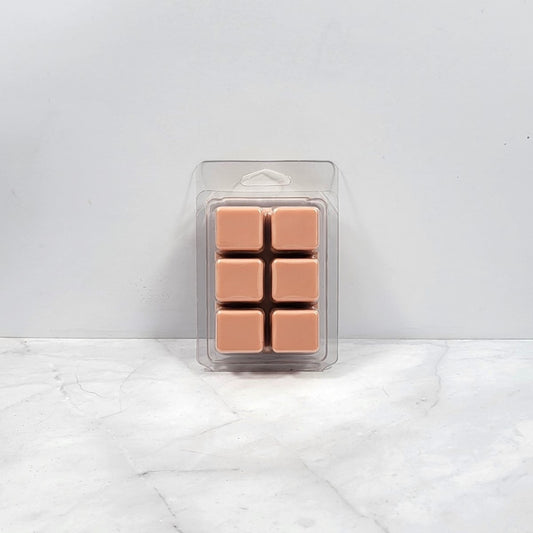 Pack of six tan-colored wax melts in clear packaging on a white marble surface with light gray background