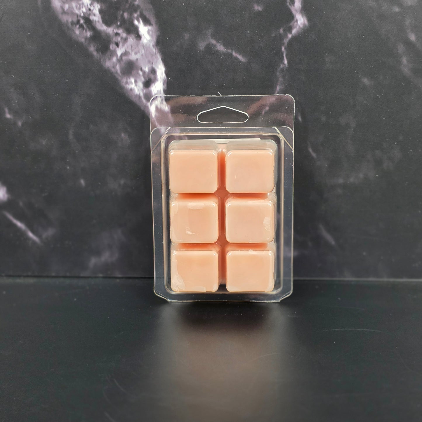 Pack of six tan-colored wax melts in clear packaging on a black marble surface