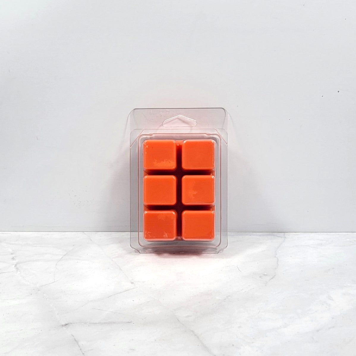 Pack of orange wax melts in a clear plastic packaging on a white marble surface.