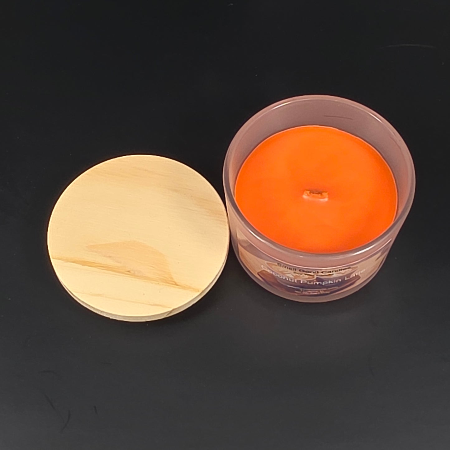 Orange candle in a clear container with a wooden lid on a black background
