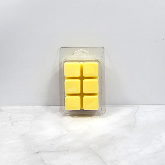 Pack of six yellow wax melts in clear packaging on a white marble surface.