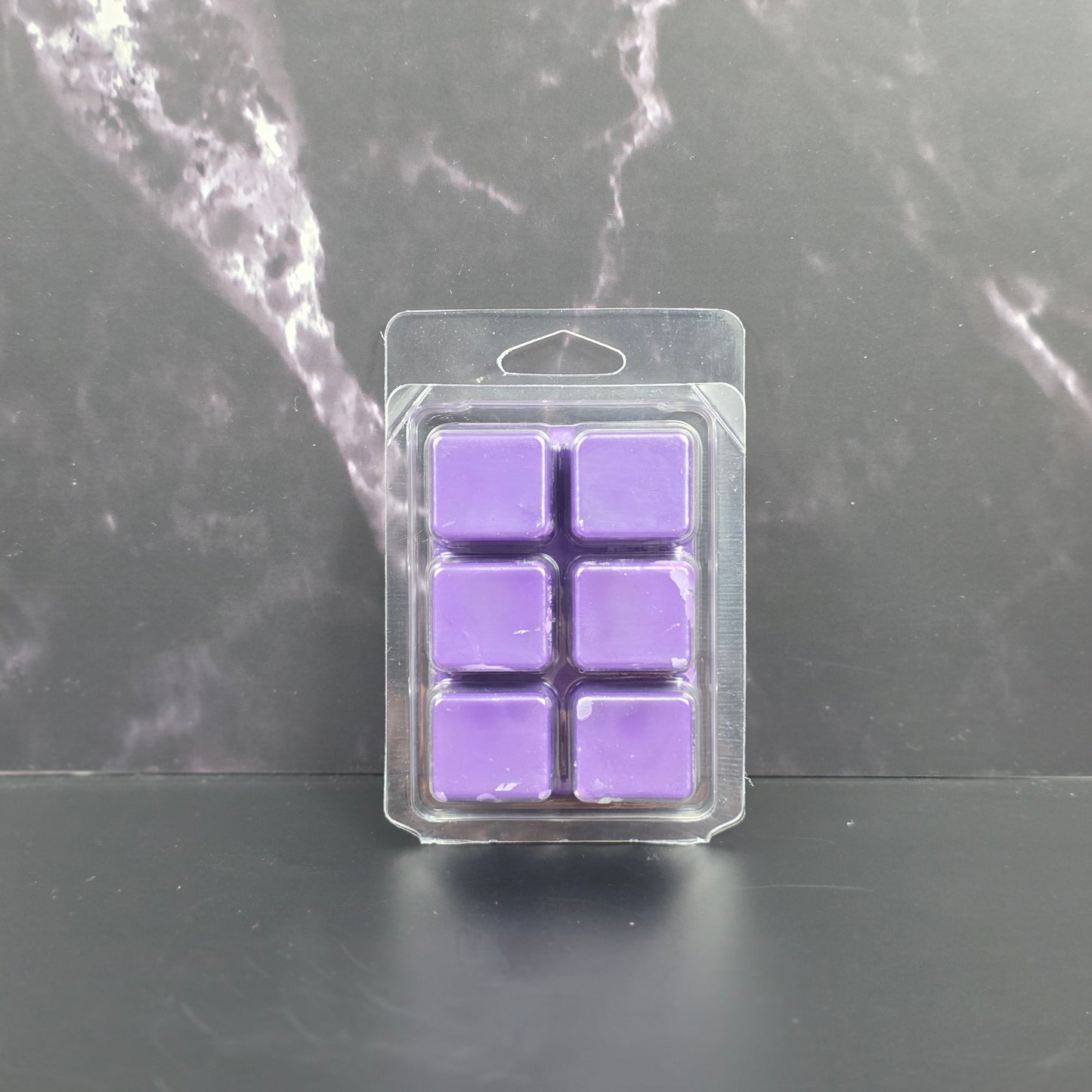 Pack of six purple wax melts in clear packaging on a dark marble surface