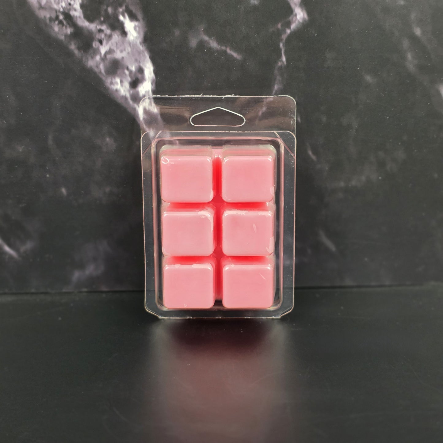 Pack of pink wax melts in clear packaging on a dark marble background