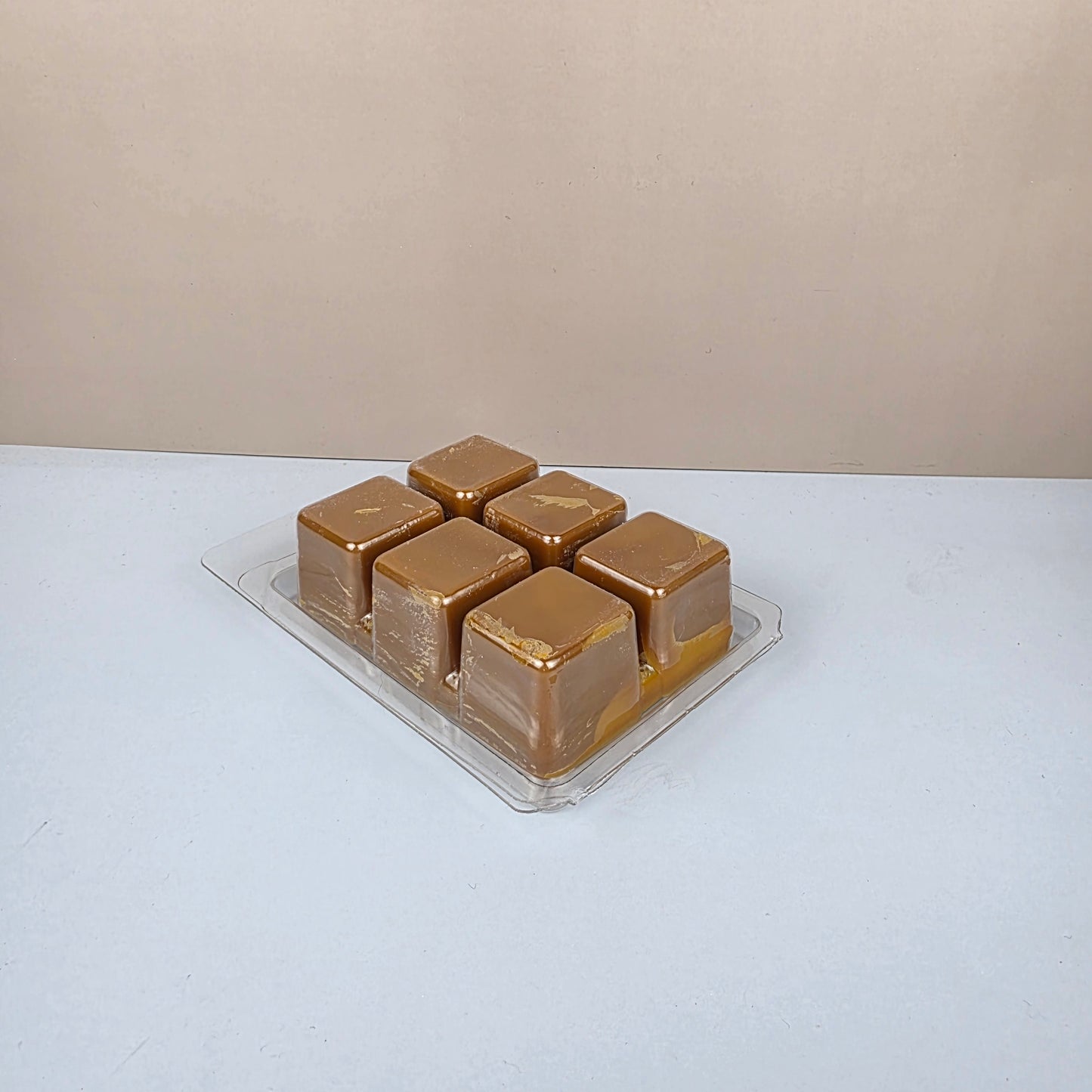 Gold-colored wax cubes in a clear plastic packaging on a white background