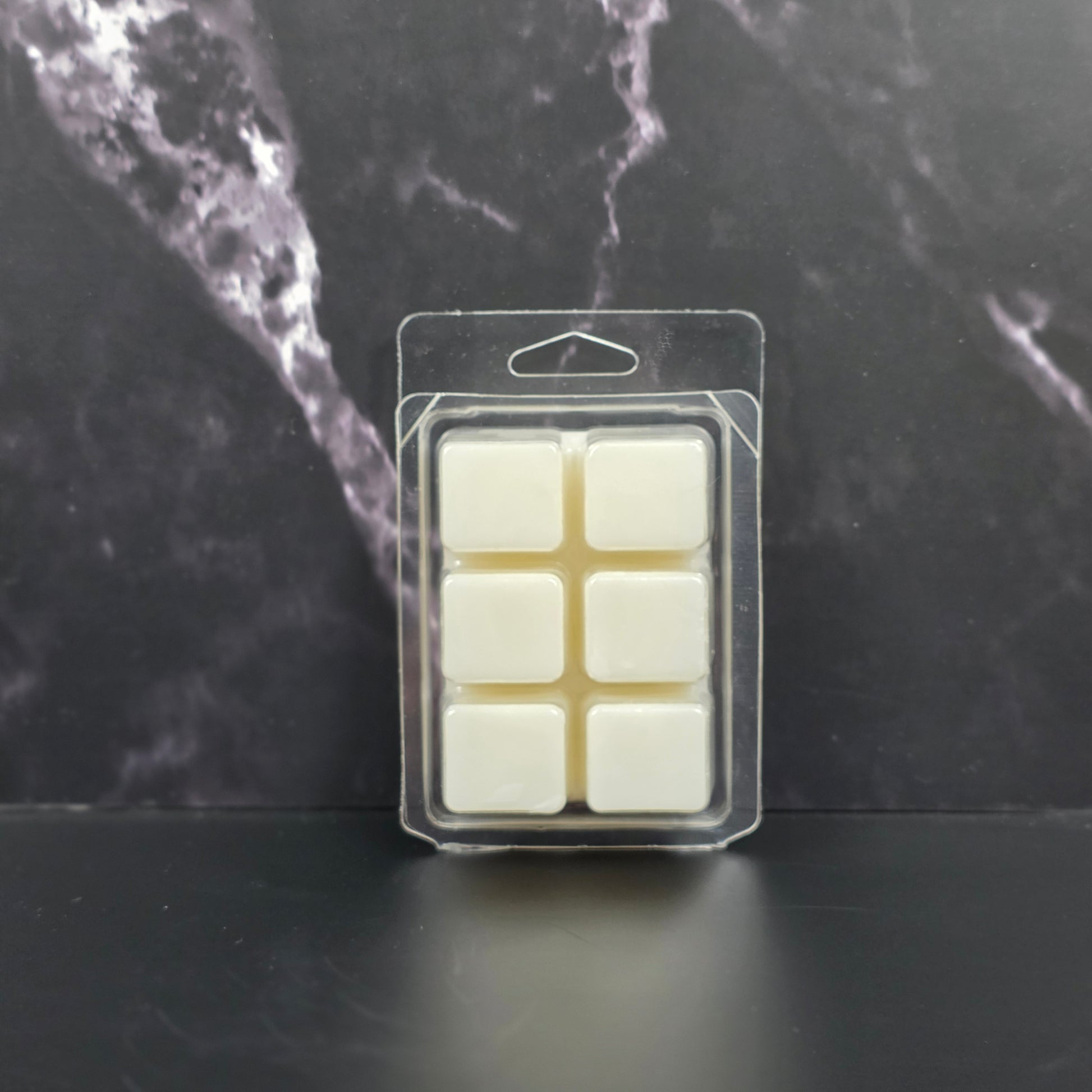 Pack of six white wax melts in clear packaging on a dark marble surface
