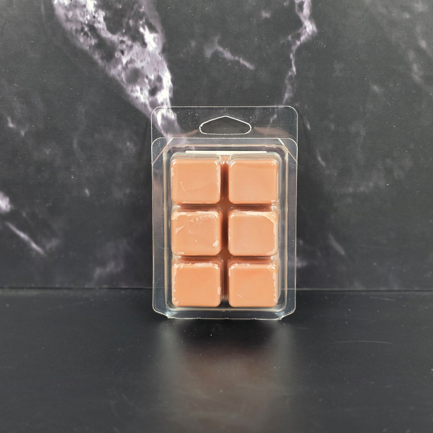Pack of peach-colored wax melts in clear packaging on a dark marble surface