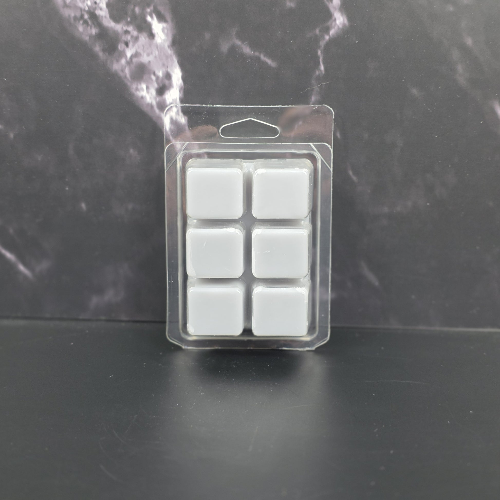 Pack of six gray wax melts in clear packaging on a dark marble background