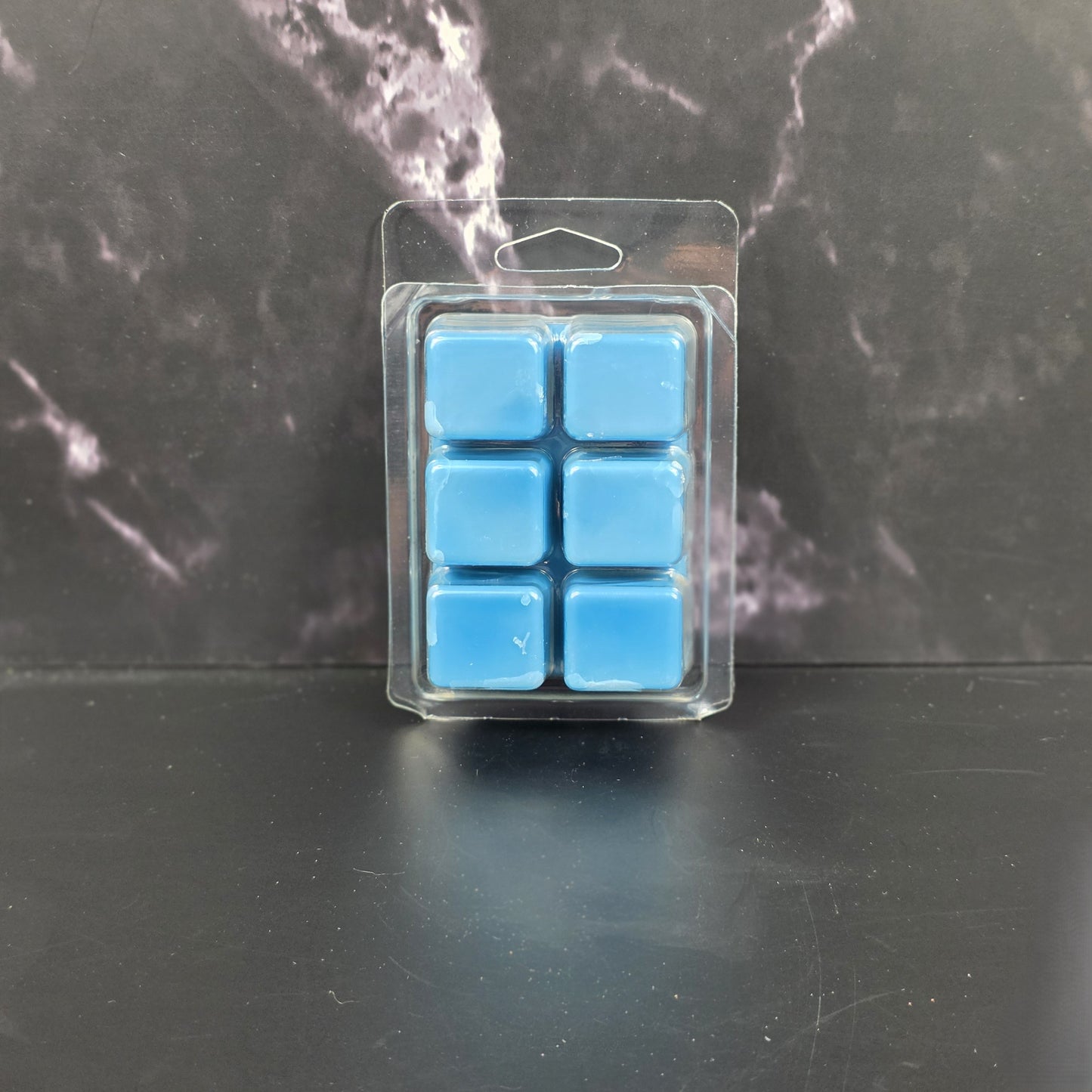 Pack of blue wax melts in clear packaging on a dark marble surface