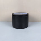 Black cylindrical container with a label on a light gray surface and beige background