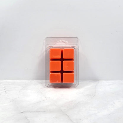 Pack of orange wax melts in a clear plastic packaging on a white marble surface.