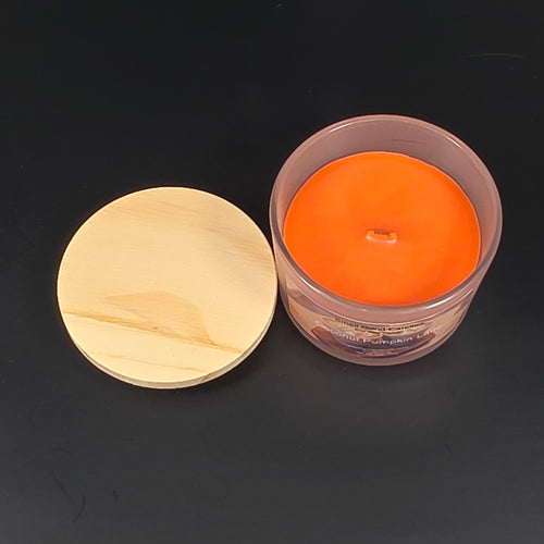 Orange candle in a clear container with a wooden lid on a black background