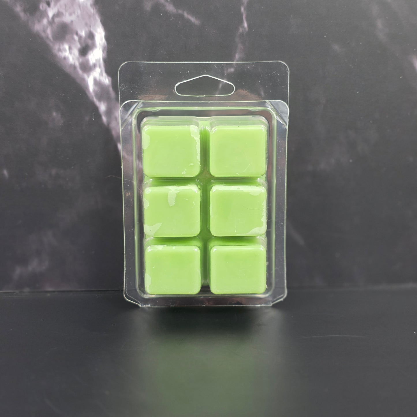 Pack of six green wax melts in clear packaging on a dark surface