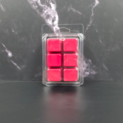 Pack of six red wax melts in clear packaging on a dark marble surface
