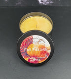 Scented candle in a tin labeled 'Fall Festival' on a dark surface