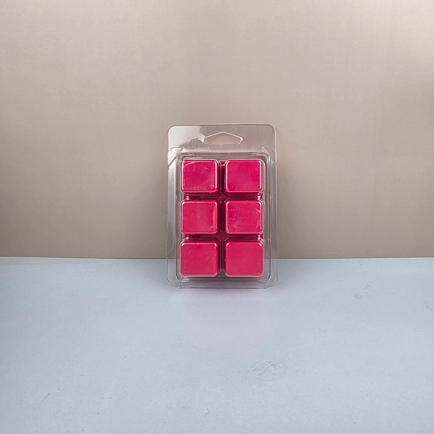 Pack of pink wax cubes in clear plastic packaging on a beige and white background