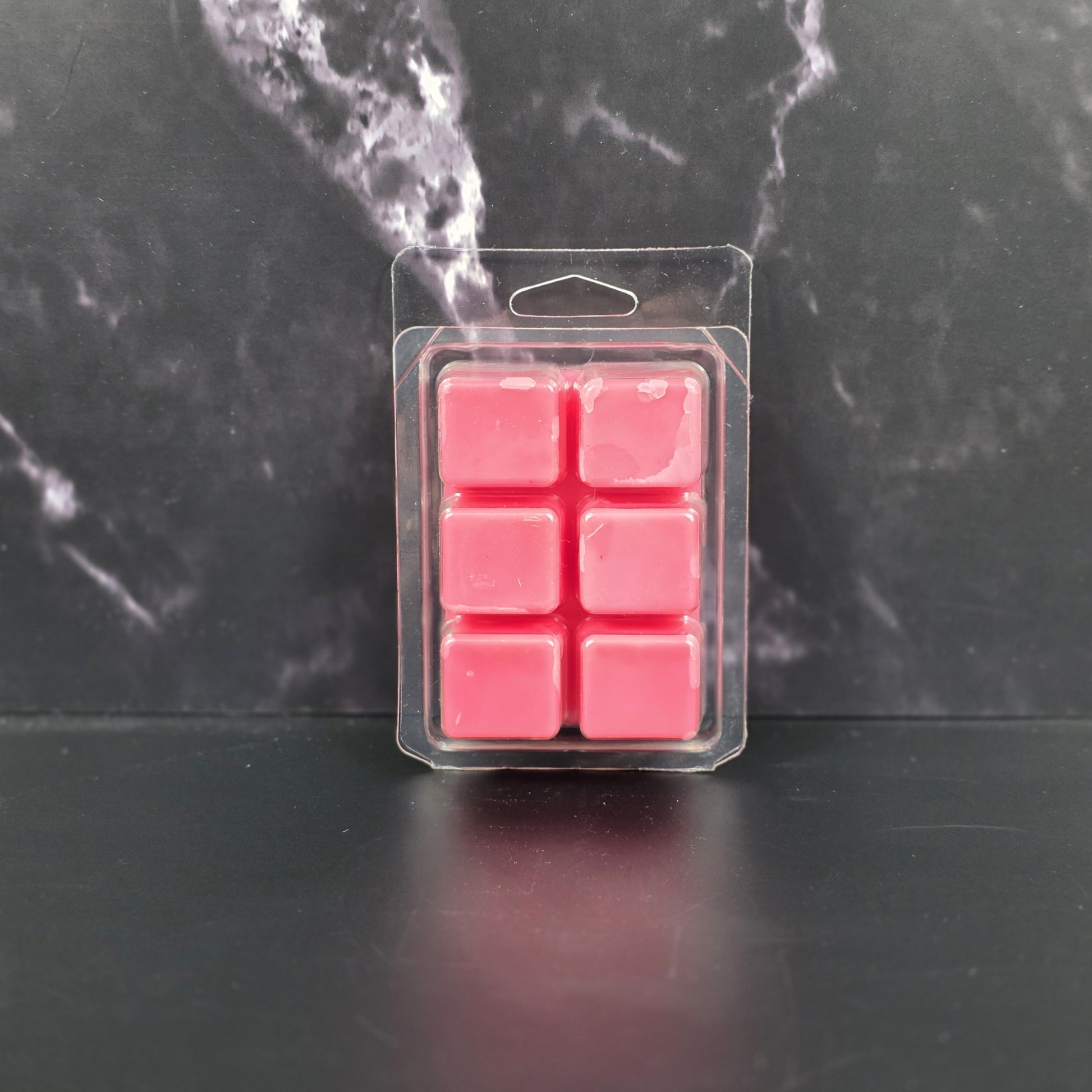 Pack of pink wax melts in clear packaging on a dark marble surface