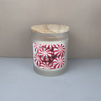 Frosted glass candle jar with wooden lid and peppermint-themed label on a neutral background