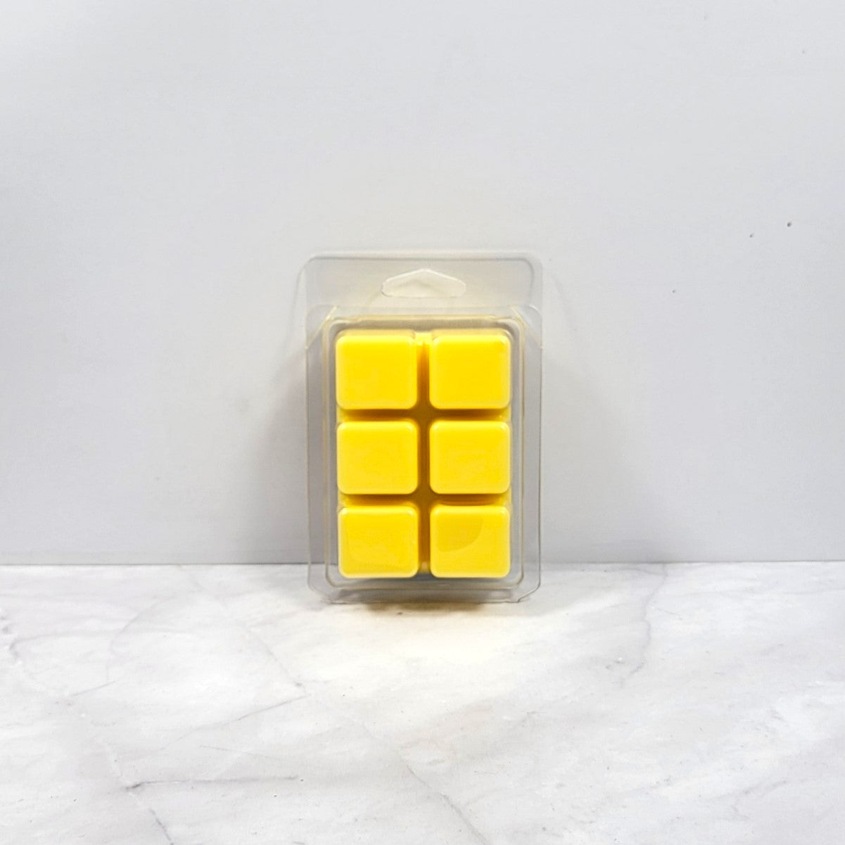 Pack of yellow wax melts in a clear plastic packaging on a white marble surface.
