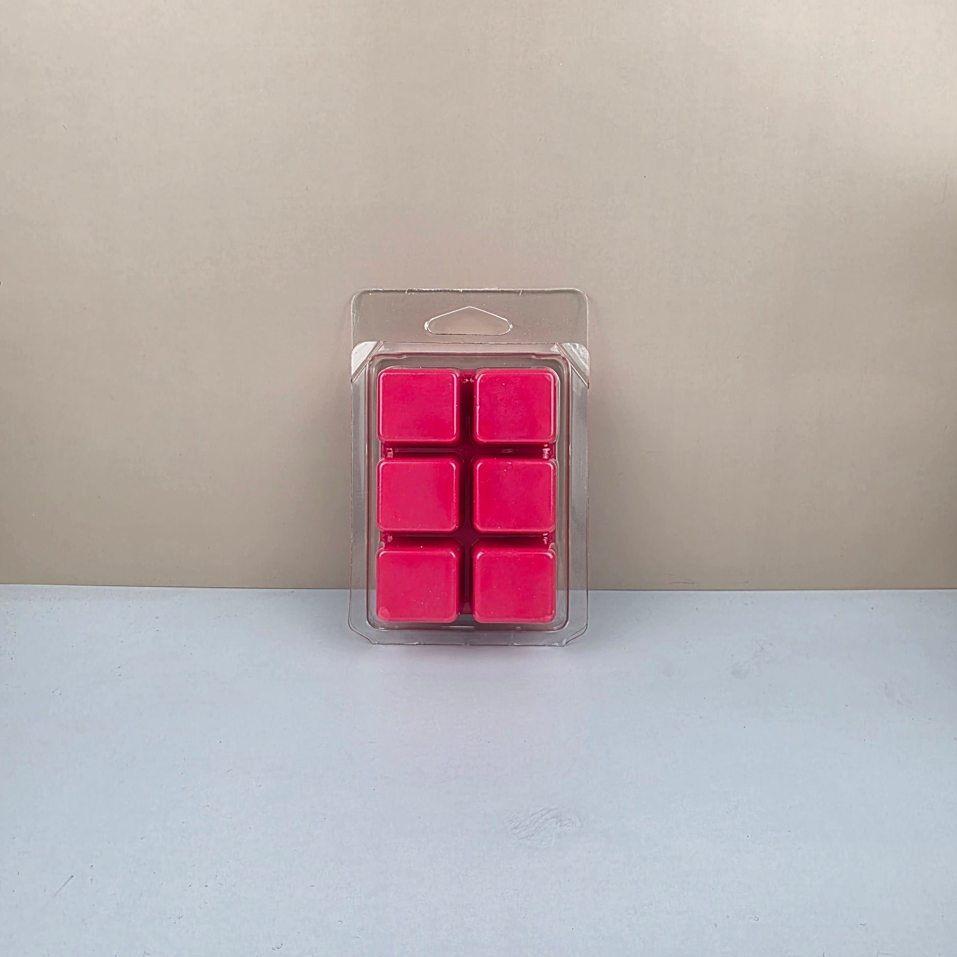 Pack of pink wax melts in a clear plastic packaging on a beige and white background