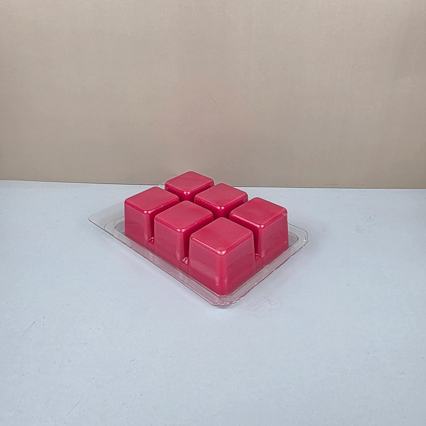 Pack of pink wax melts in a clear plastic packaging on a beige and white background