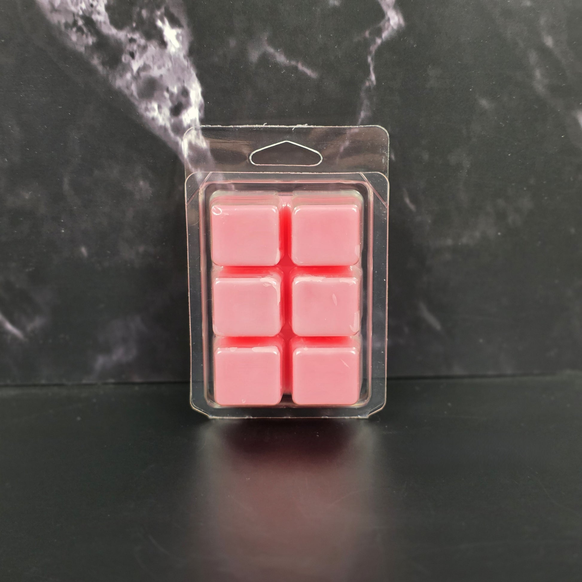 Pack of pink wax melts in clear packaging on a dark marble background