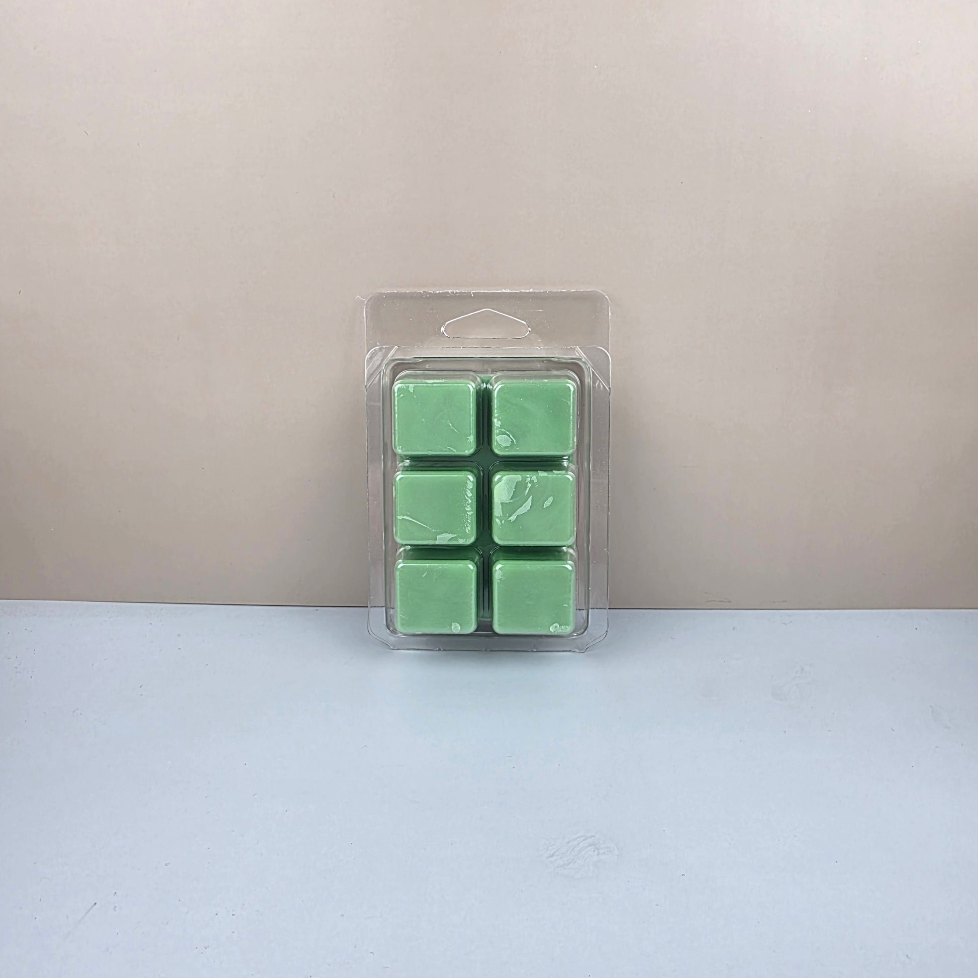 Pack of six green wax melts in a clear plastic packaging on a light gray background