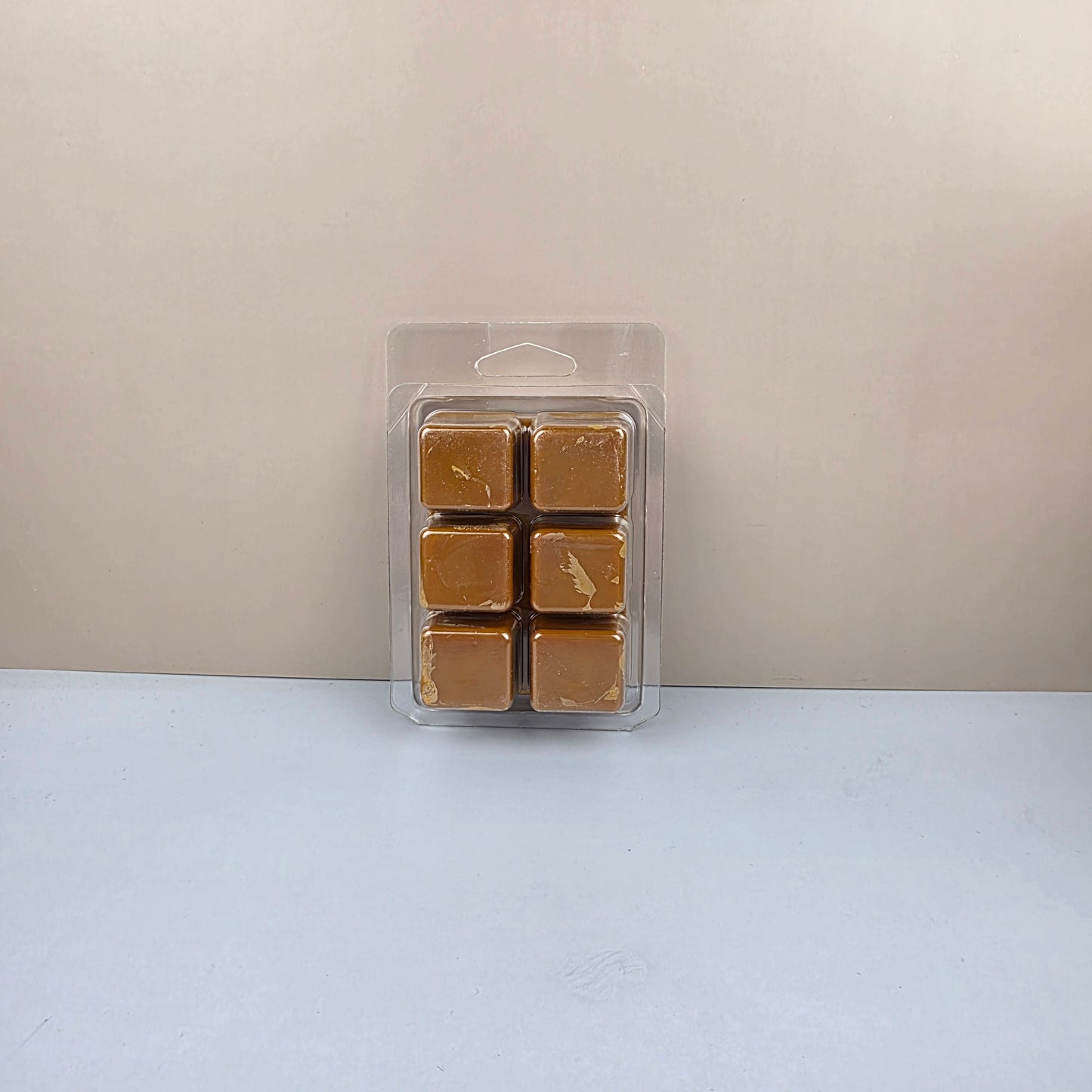 Pack of six brown wax melts in a clear plastic packaging on a light gray background