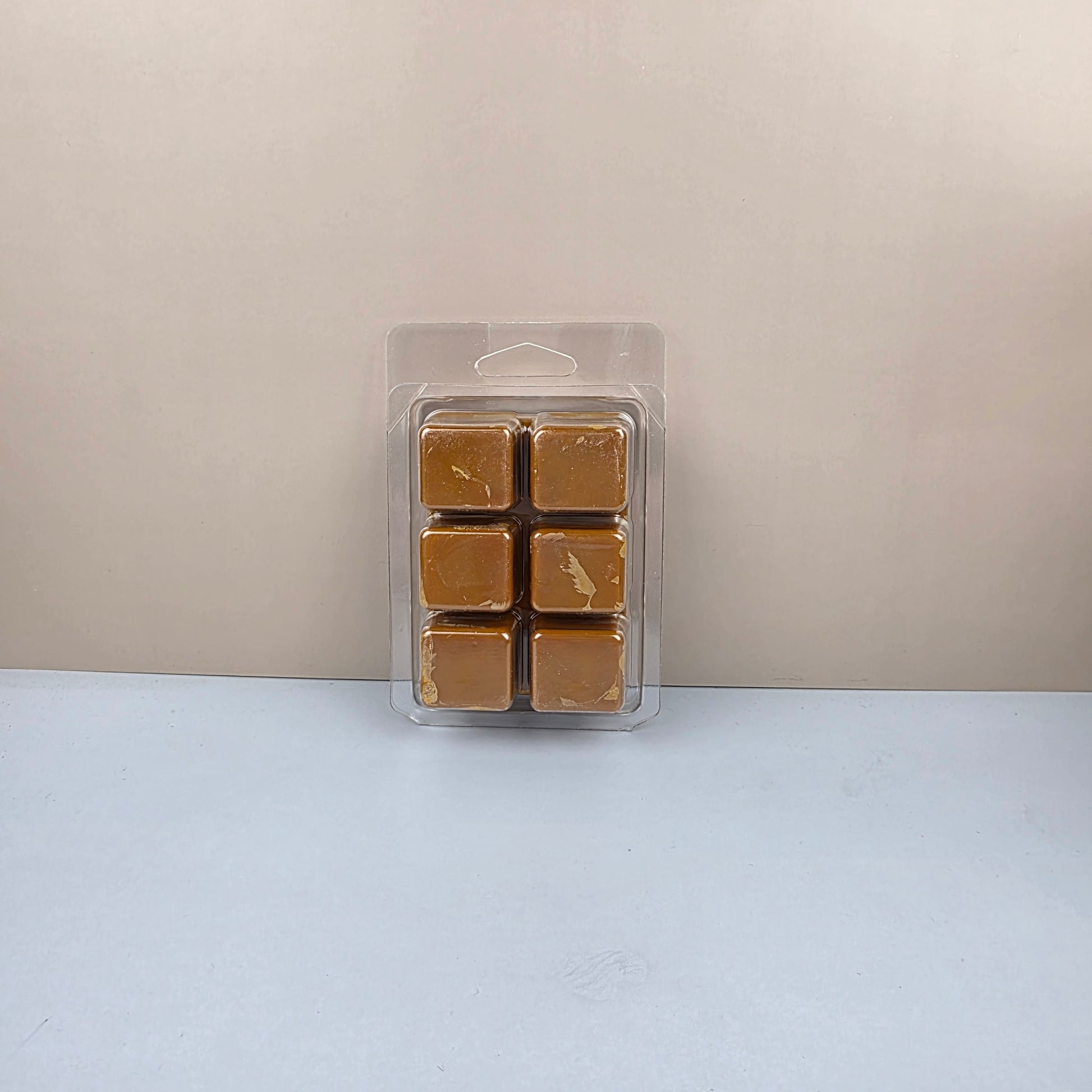 Pack of six brown wax melts in a clear plastic packaging on a light gray background