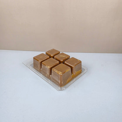 Gold-colored wax cubes in a clear plastic packaging on a white background