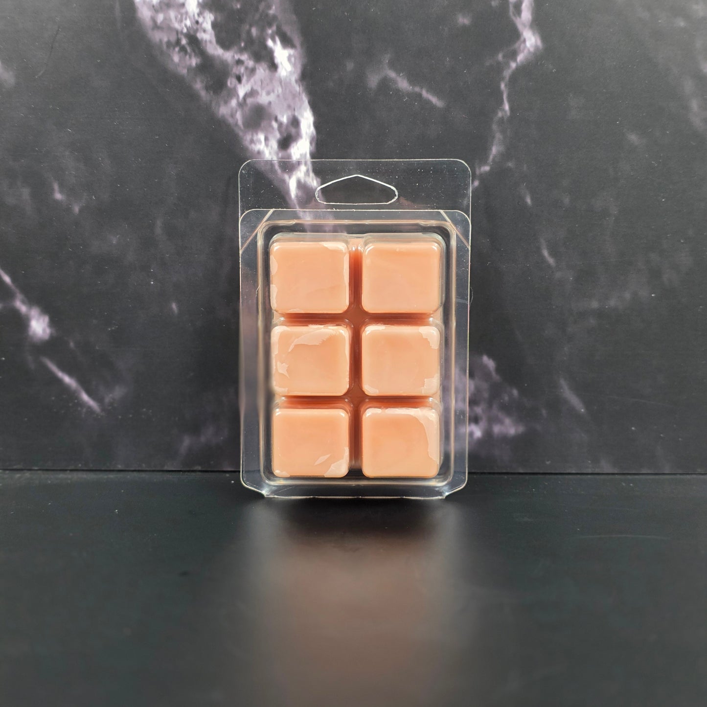 Pack of six peach-colored wax melts in clear packaging on a dark marble surface