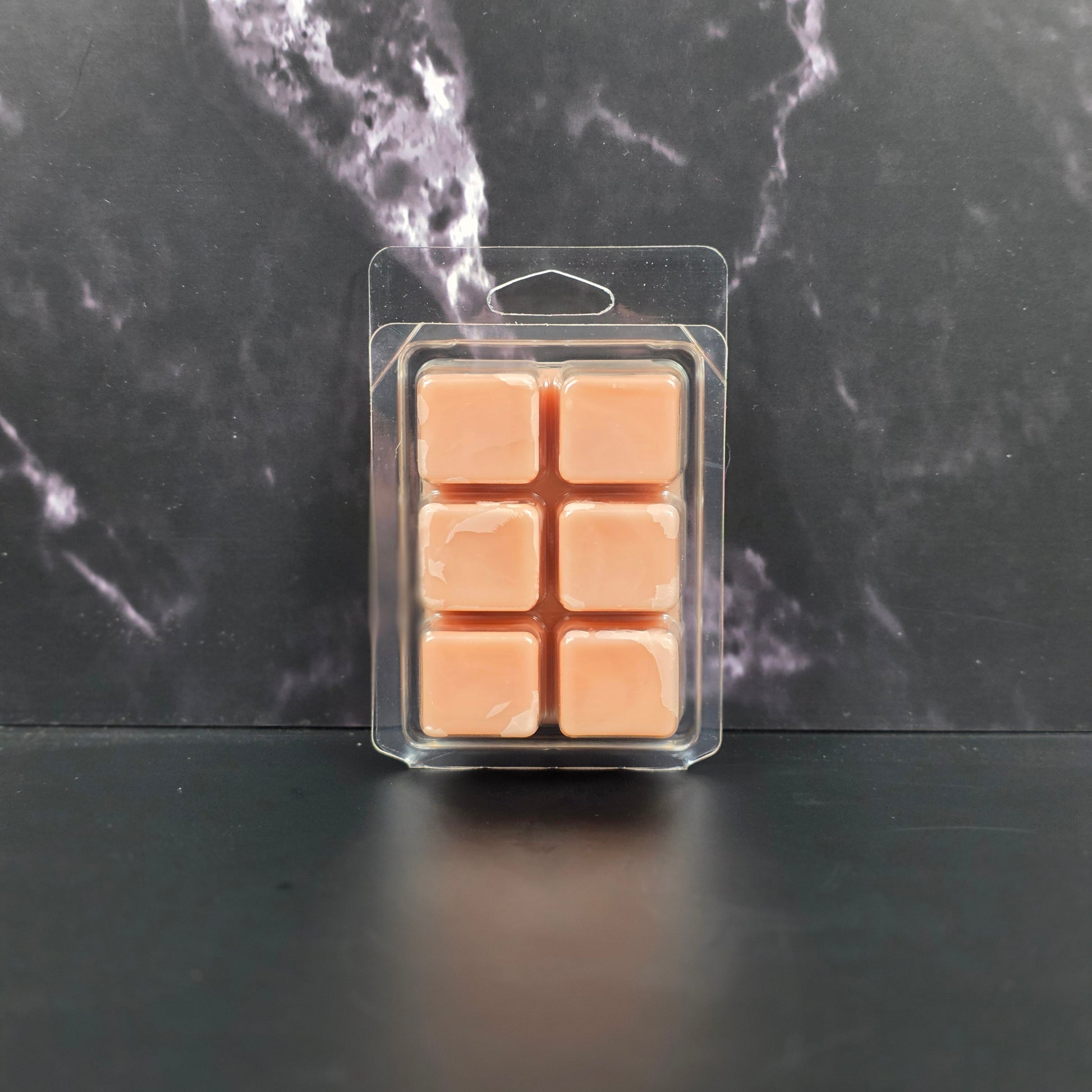 Pack of six peach-colored wax melts in clear packaging on a dark marble surface