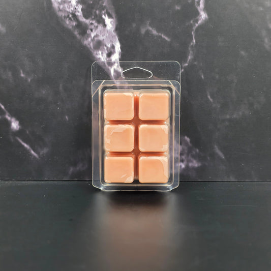 Pack of six peach-colored wax melts in clear packaging on a dark marble surface